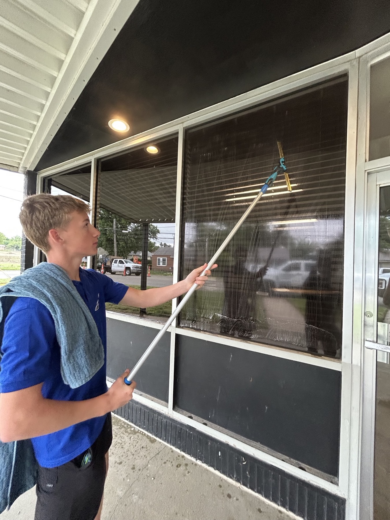 Technician cleaning large storefront windows under an awning