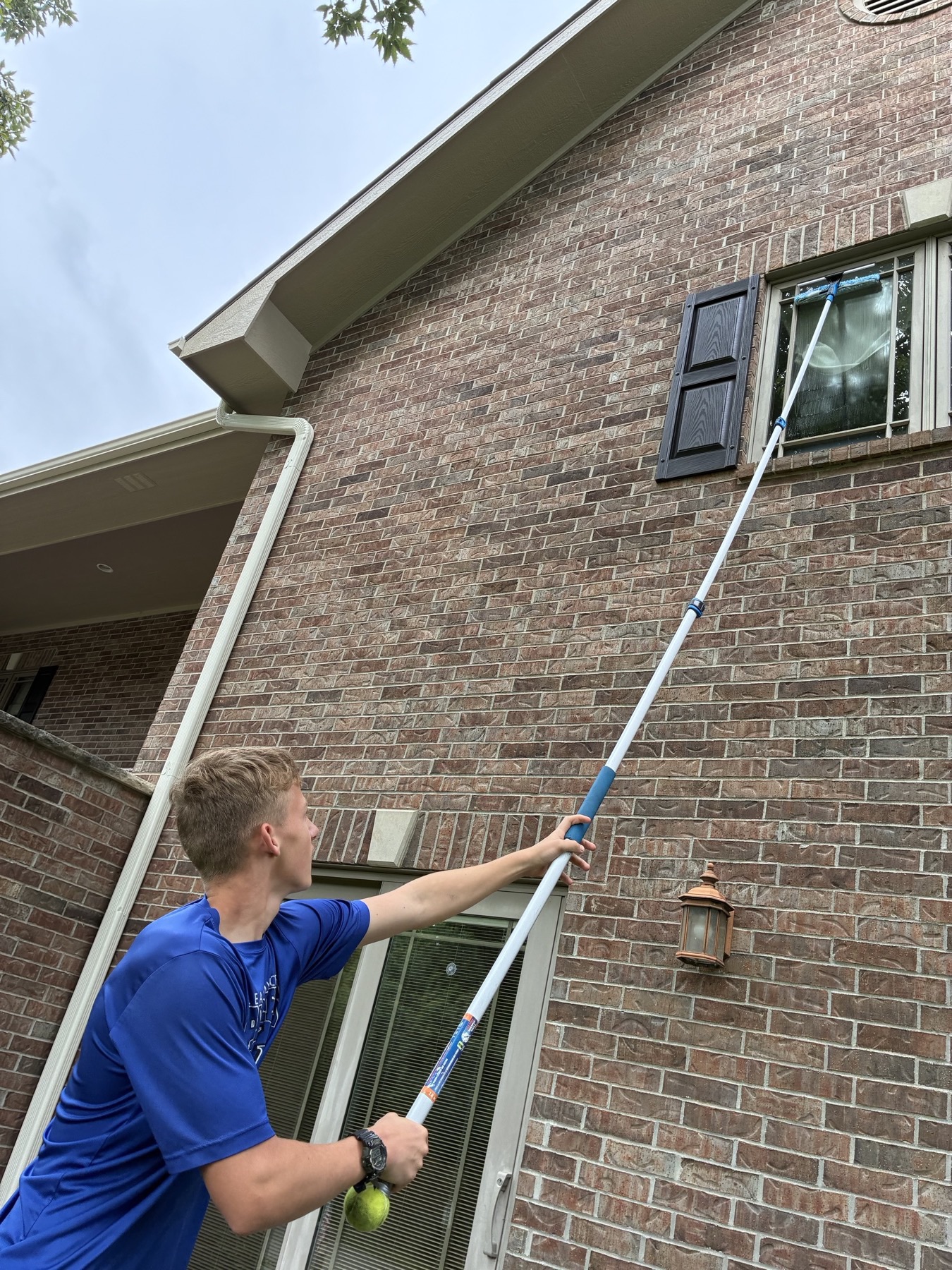 Technician cleaning a second-story window on a brick home with a water-fed pole